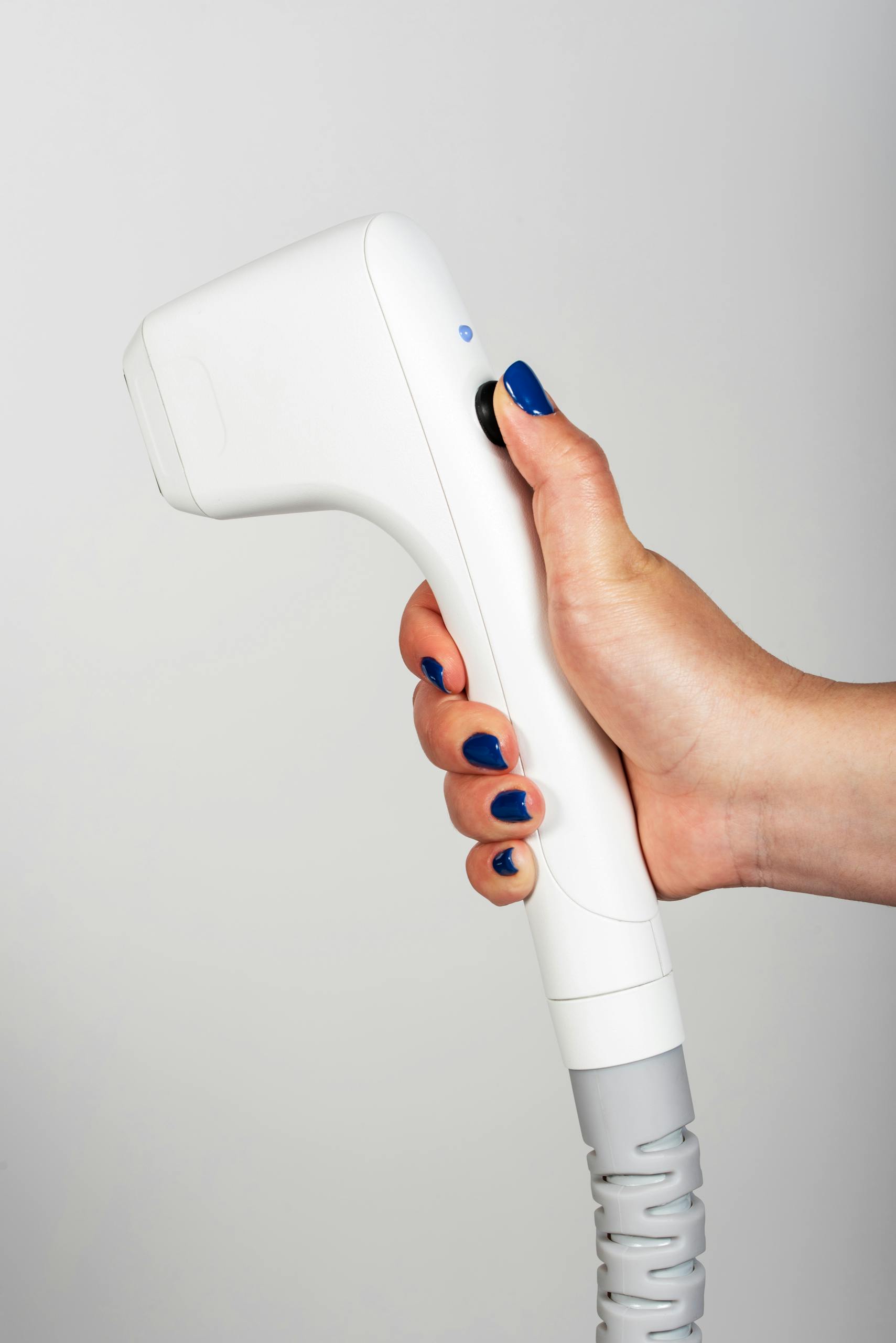 Close-up of a female hand holding a white ultrasound device against a white background.
